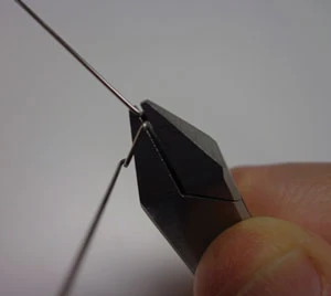 Technician bending stainless steel orthodontic wire with Adams pliers on the laboratory bench